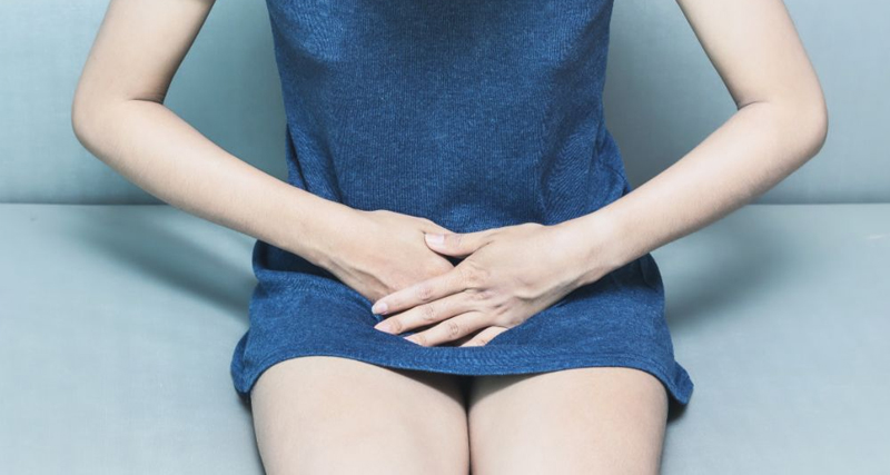 Woman sitting and holding lower abdomen, symbolising discomfort from bacterial vaginosis (BV).