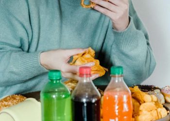 Person eating fast food and sugary snacks, surrounded by fizzy drinks and pastries, representing binge eating disorder (BED) behaviour.