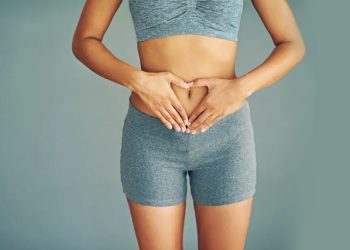 Woman in fitness clothing forming a heart shape with hands over lower abdomen, symbolising bladder health awareness.