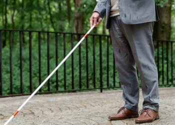 Man in formal attire using a white cane for navigation, symbolising blindness or vision loss.