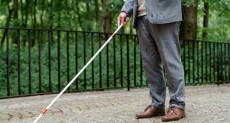 Man in formal attire using a white cane for navigation, symbolising blindness or vision loss.