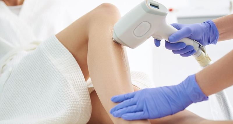 A medical professional uses a skincare device on a woman's leg during a treatment session to promote long-term skin health.