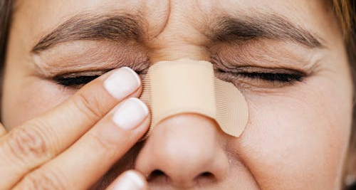 Woman touching nose with plaster bandage – broken nose pain