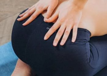 Woman kneeling on a mat while holding her lower back in discomfort