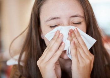 Woman sneezing into a tissue due to catarrh symptoms