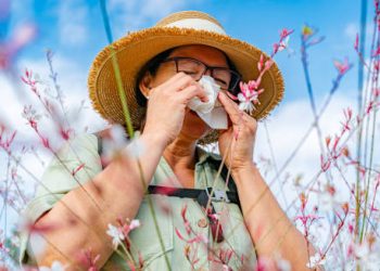 Woman sneezing in a field of flowers due to seasonal allergies