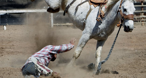 Man falling off a horse during a rodeo event, illustrating a traumatic back injury risk