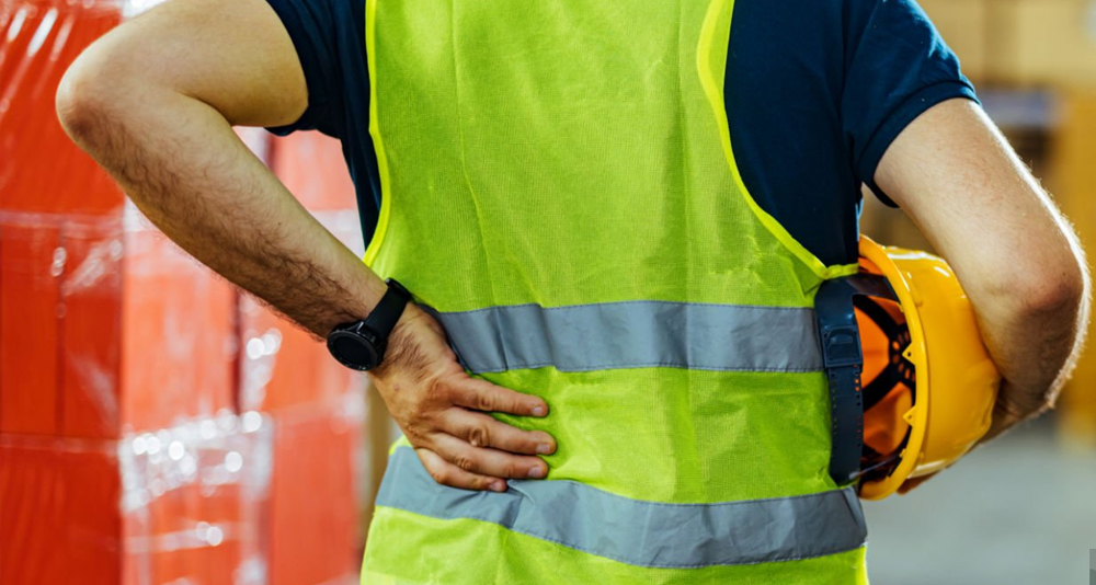 Construction worker holding lower back in pain while wearing a reflective vest