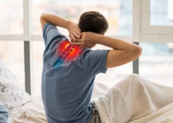 Man sitting on bed holding neck with highlighted spine pain