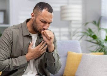 Man coughing and holding chest in discomfort at home