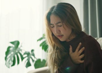 Woman clutching chest in pain while sitting on a couch
