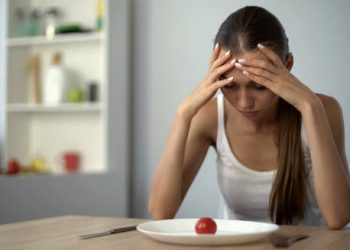 Woman staring at a single cherry tomato on a plate with her head in her hands