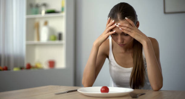 Woman staring at a single cherry tomato on a plate with her head in her hands