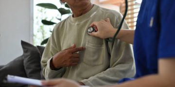 Doctor using stethoscope to examine patient's chest during heart check-up
