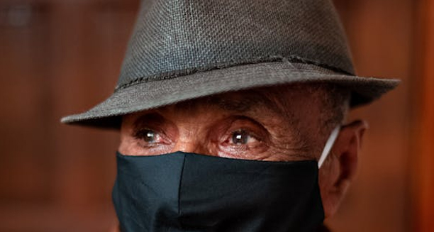 Elderly man wearing a hat and face mask with visible eye complications