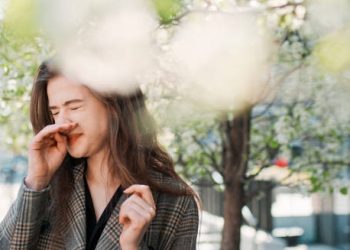 Woman sneezing outdoors during allergy season