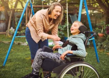 Child in a wheelchair smiling with caregiver in a sunny park