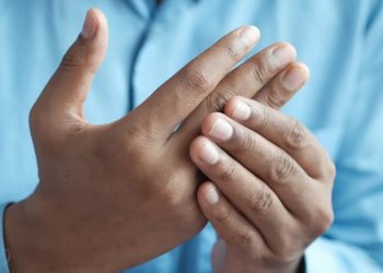 Man holding his injured finger in pain while wearing a blue shirt