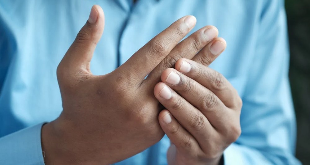 Man holding his injured finger in pain while wearing a blue shirt