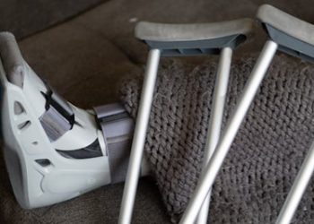 Person with a broken leg resting on a couch with crutches and a medical walking boot