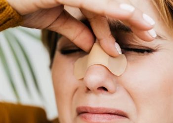 Woman holding her nose with a bandage across the bridge