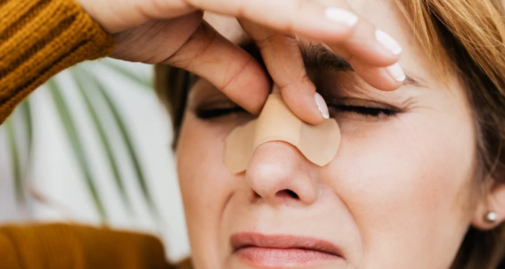 Woman holding her nose with a bandage across the bridge