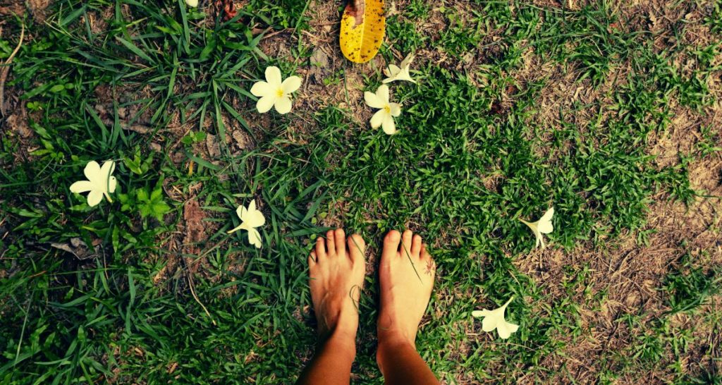 Bare feet standing on grass surrounded by flowers as a calming mindfulness exercise