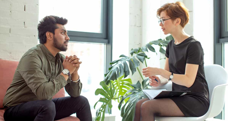 A man speaking with a female mental health professional during a counselling session in a modern, bright office.