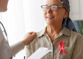 Smiling cancer patient with pink ribbon talking to doctor