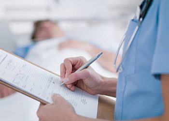 Medical professional writing on a patient chart in a hospital setting