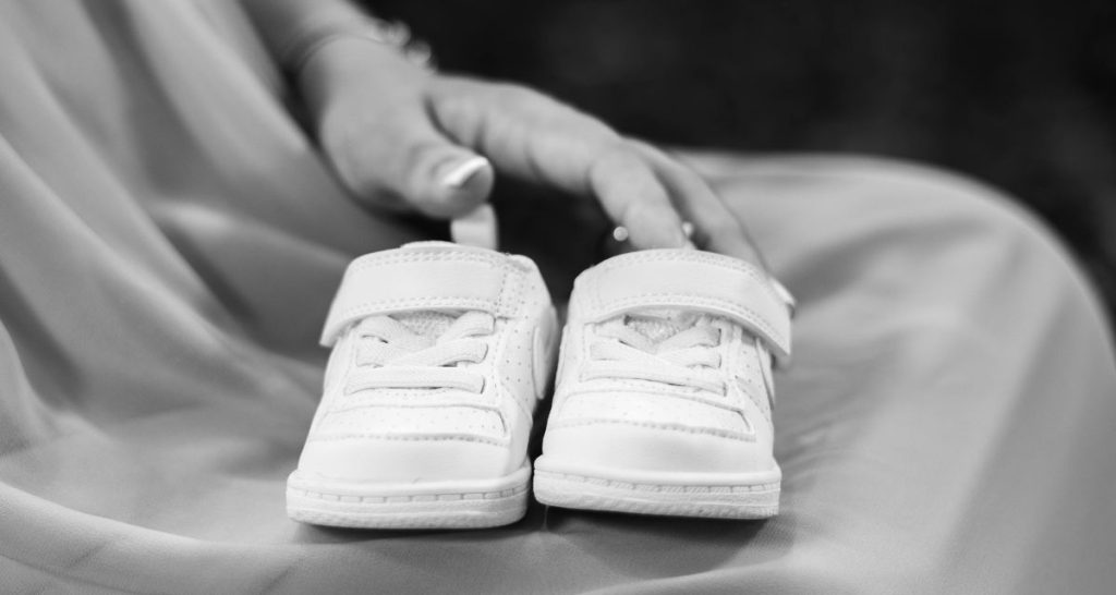 Small white baby shoes on a person's lap