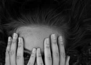 Black and white photo of a woman partially covering her face with her hands, expressing emotion or introspection.