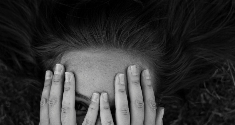 Black and white photo of a woman partially covering her face with her hands, expressing emotion or introspection.