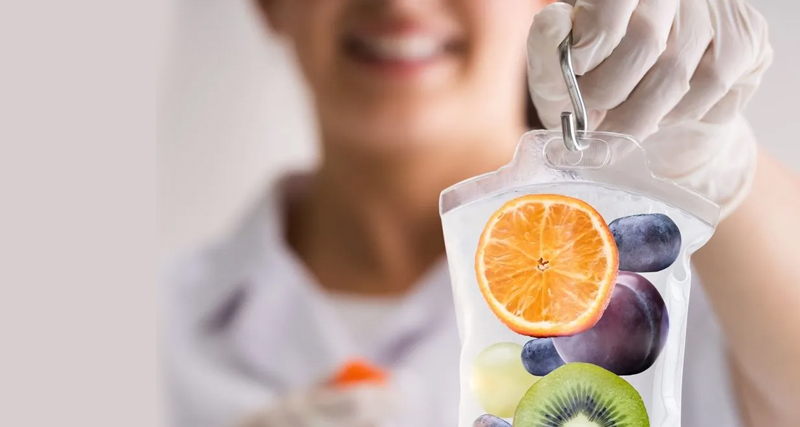 Smiling healthcare provider holding IV bag filled with images of fruits, symbolising nutritional therapy for bile duct cancer support.