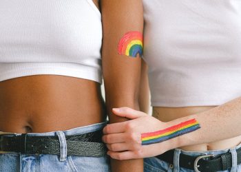 Two women standing arm-in-arm showing LGBTQ+ pride with rainbow body art