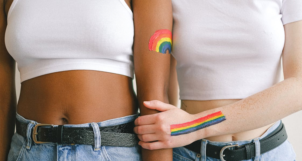Two women standing arm-in-arm showing LGBTQ+ pride with rainbow body art