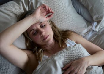 Woman lying in bed appearing feverish and fatigued