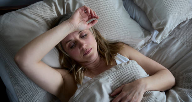 Woman lying in bed appearing feverish and fatigued