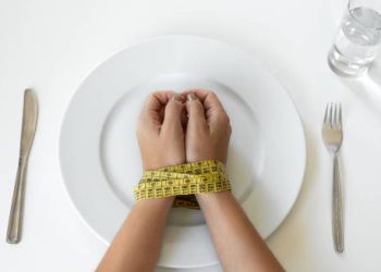 Hands tied with measuring tape over an empty plate, symbolising eating disorder
