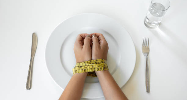 Hands tied with measuring tape over an empty plate, symbolising eating disorder