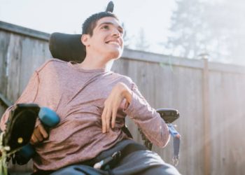 Young man in a motorised wheelchair smiling outdoors