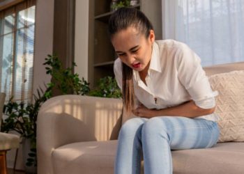 Woman experiencing abdominal pain while sitting on a couch