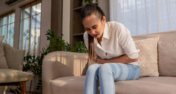 Woman experiencing abdominal pain while sitting on a couch