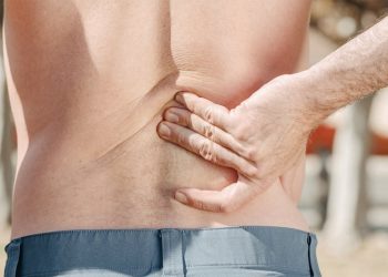 Man clutching lower back in pain, indicating possible spinal fracture symptoms