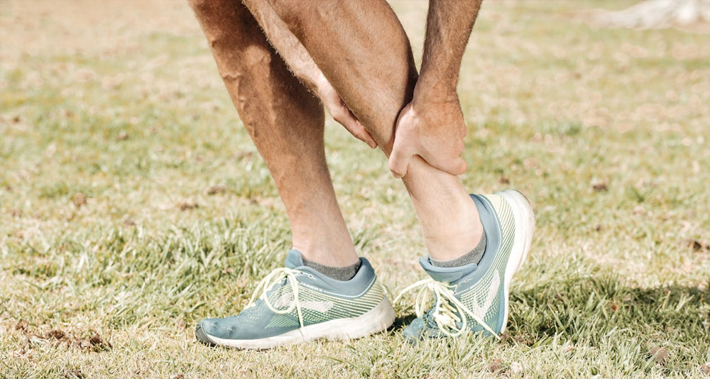 Man holding his lower leg in pain on a grassy field