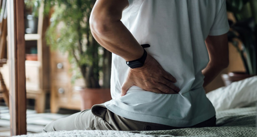 Person sitting on bed and holding lower back due to tailbone pain