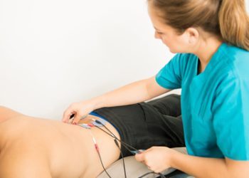 A physiotherapist applies electrodes to a man's lower back as part of bladder pain syndrome treatment.