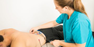 A physiotherapist applies electrodes to a man's lower back as part of bladder pain syndrome treatment.