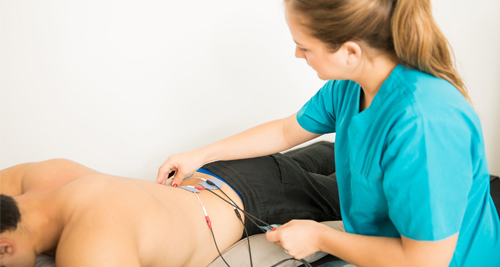 A physiotherapist applies electrodes to a man's lower back as part of bladder pain syndrome treatment.