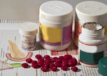 Various medicine bottles and tablets placed on an open medical textbook displaying a diagram of the urinary tract.
